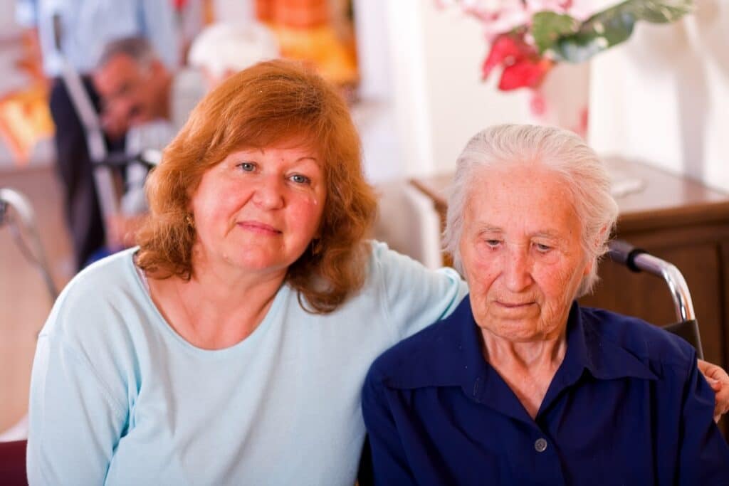 adult daughter sitting next to senior mother in nursing home