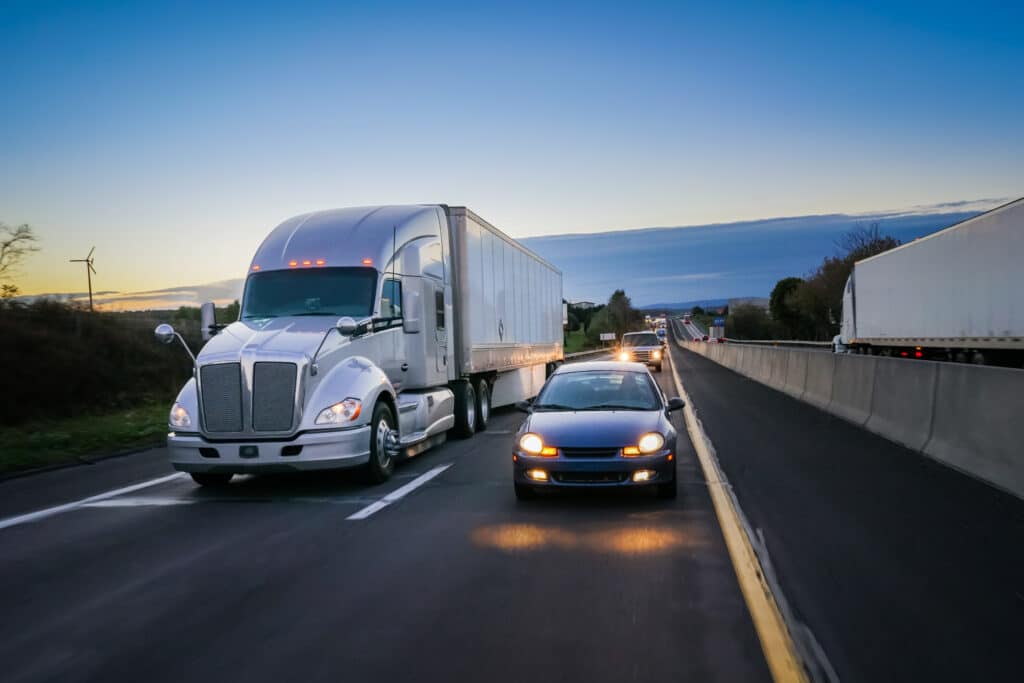 Big rig truck and passenger vehicle driving next to each other on a highway